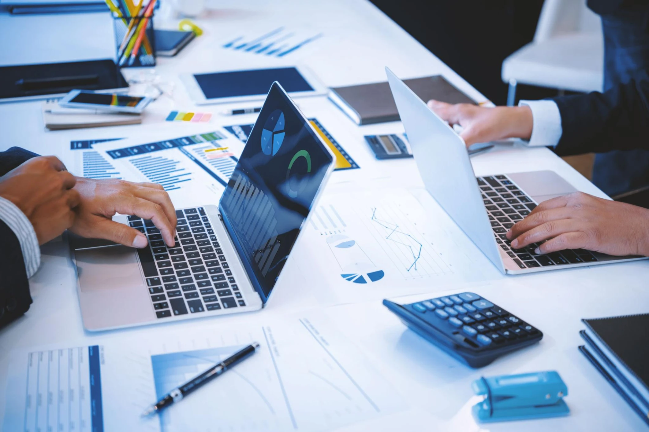 Two people working on laptops with documents.