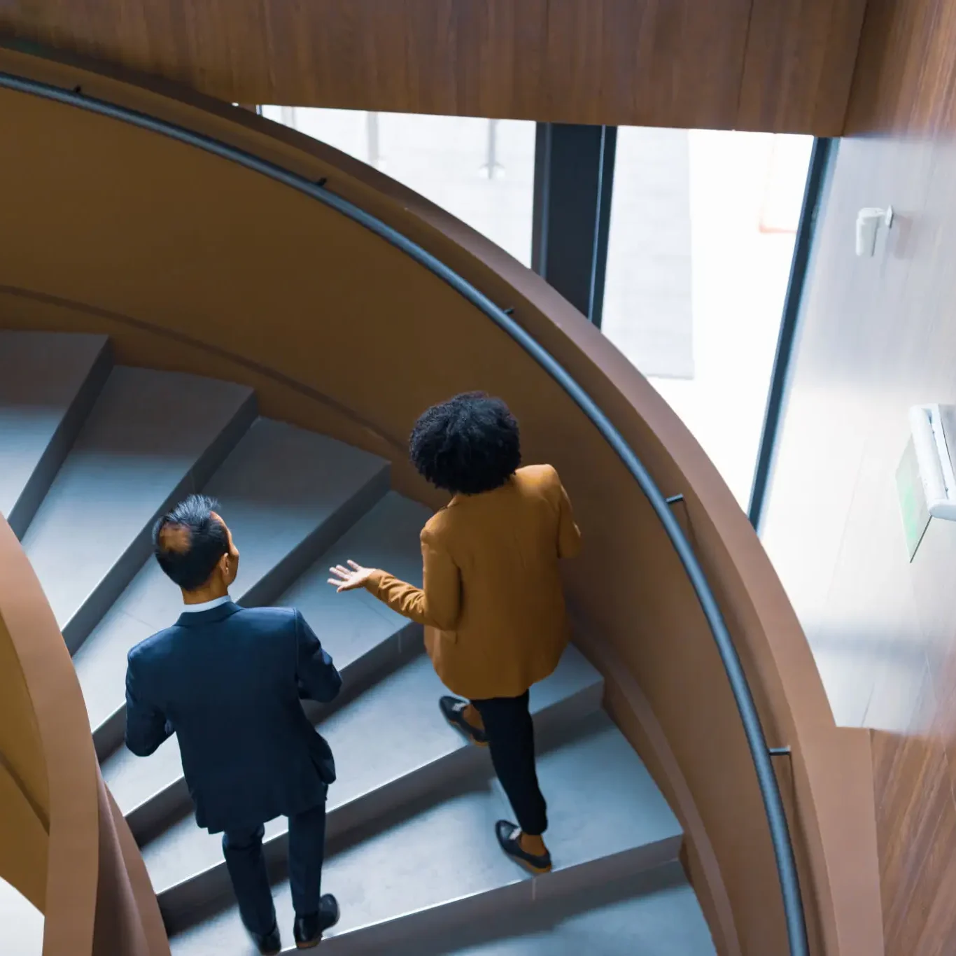 Two professionals walking down spiral staircase.